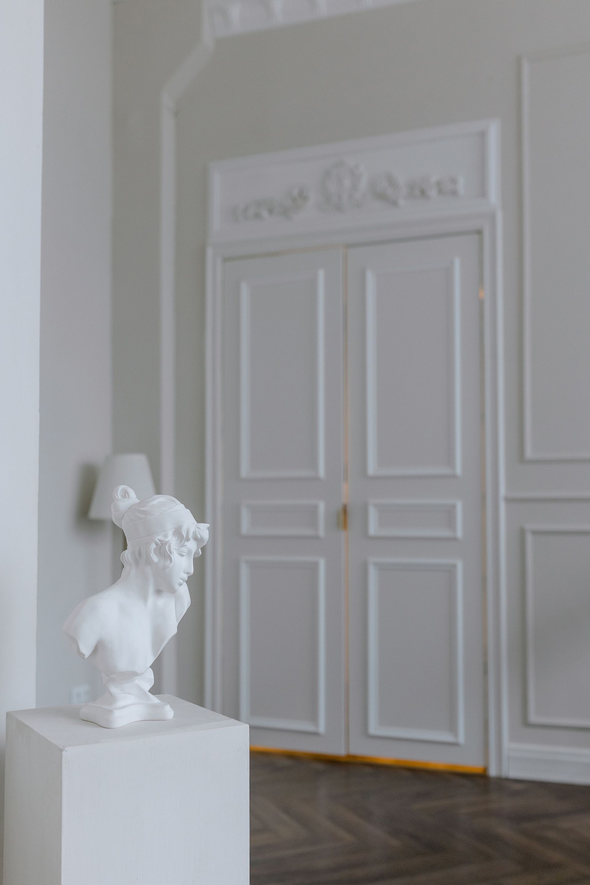 Classic white interior featuring a decorative bust and ornate double doors, exuding elegance.